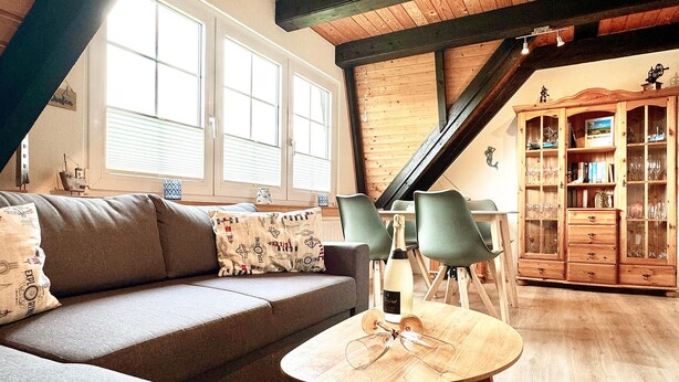 A cozy living room with a sofa, two chairs, a wooden table with wine glasses, and a wooden cabinet with glass doors.