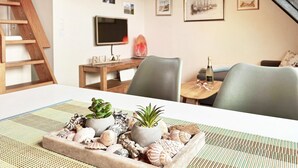 A dining area with a table set with seashells and plants, a wooden ladder, a TV, and framed pictures on the wall.