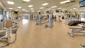 Une salle de sport spacieuse équipée de divers appareils d’exercice, de miroirs et d’un écran de télévision.