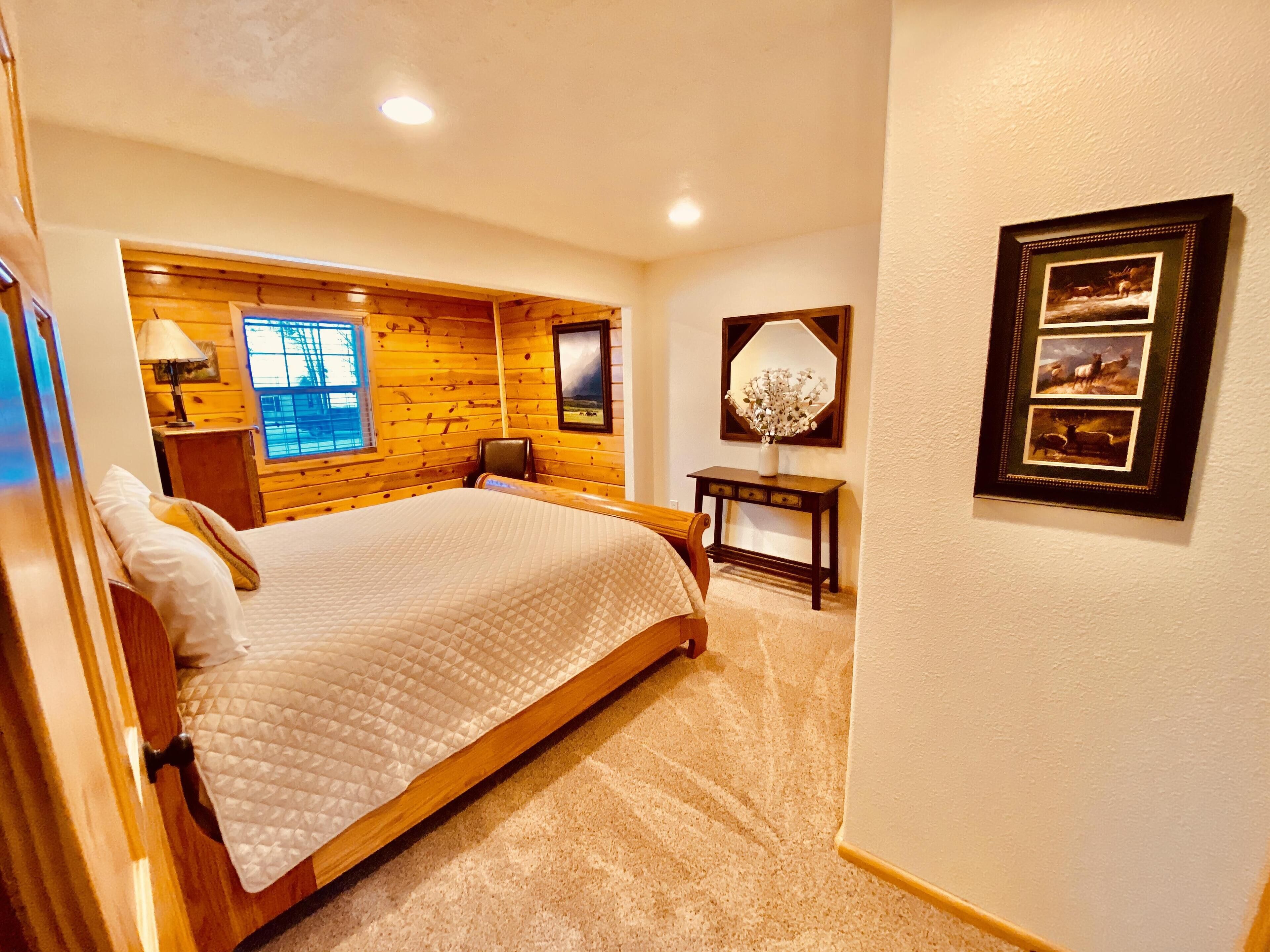 A bedroom with a large bed, wooden paneling on the walls, a desk with a lamp, and a framed picture on the wall.