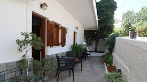 Pequeño patio al aire libre con una mesa y sillas, rodeado de plantas en macetas.