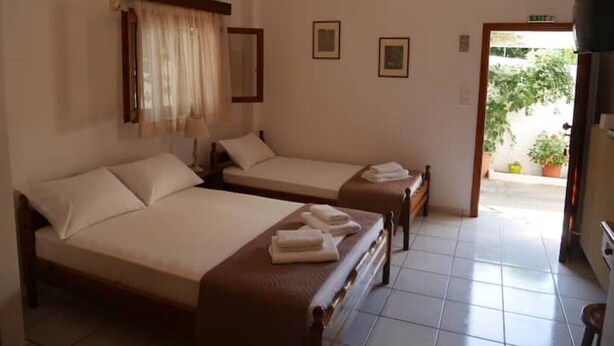 Habitación de hotel con dos camas individuales, una mesita pequeña, una lámpara colgante y vistas al exterior.