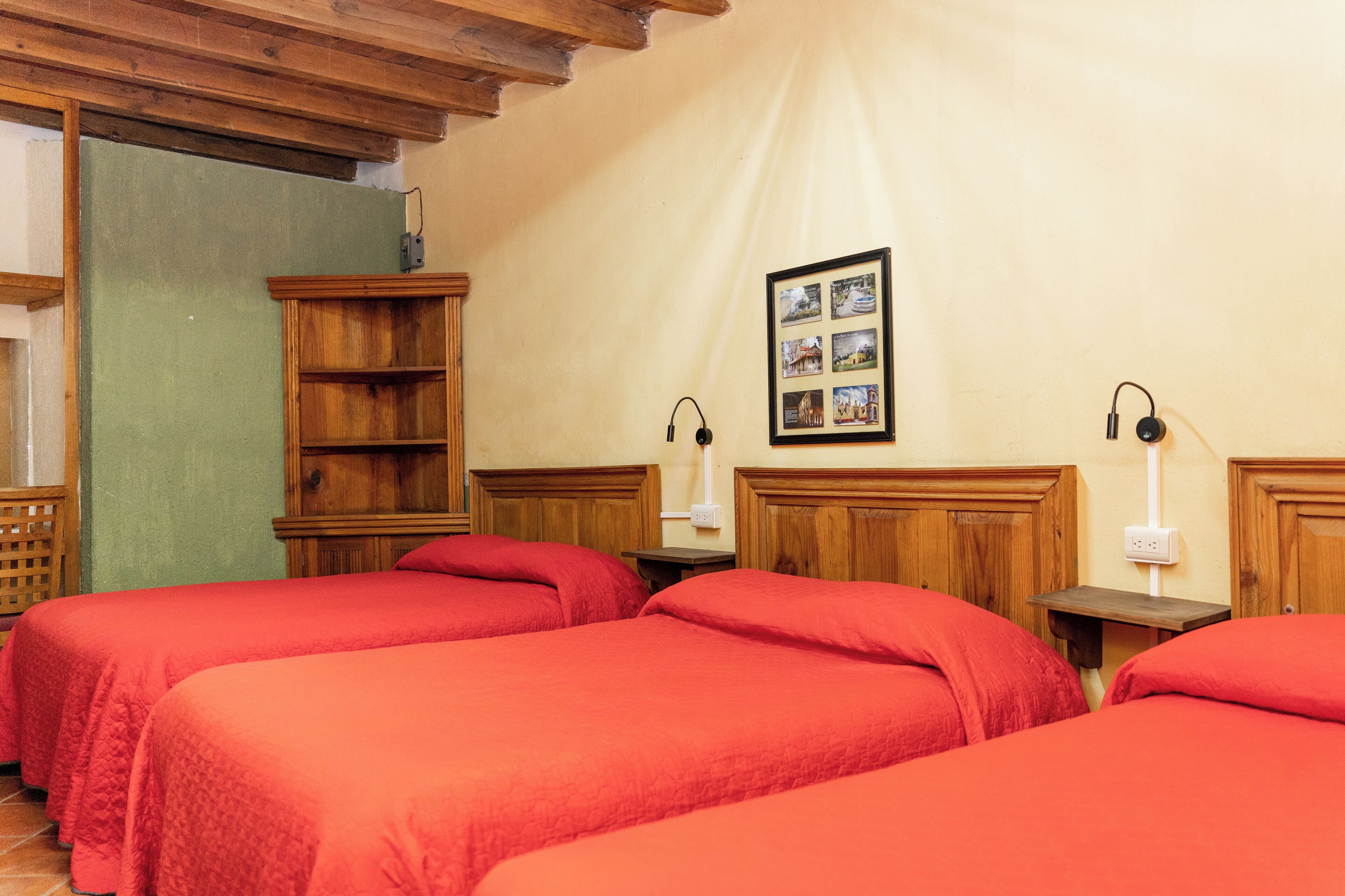 A hotel room with two single beds, wooden headboards, a small wooden nightstand with a lamp, a wooden wardrobe, and a framed photo on the wall.