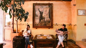 Une pièce avec un sol carrelé, des poutres en bois au plafond, un grand tableau accroché au mur et une plante en pot.
