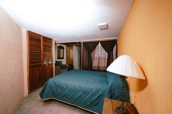 Un dormitorio con cama, un armario de madera, escritorio, lámpara y ventana con cortinas.