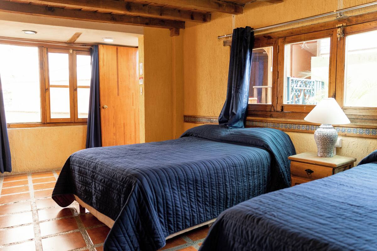 Une chambre avec deux lits, des murs en bois, une fenêtre avec des rideaux et une table de chevet avec une lampe.