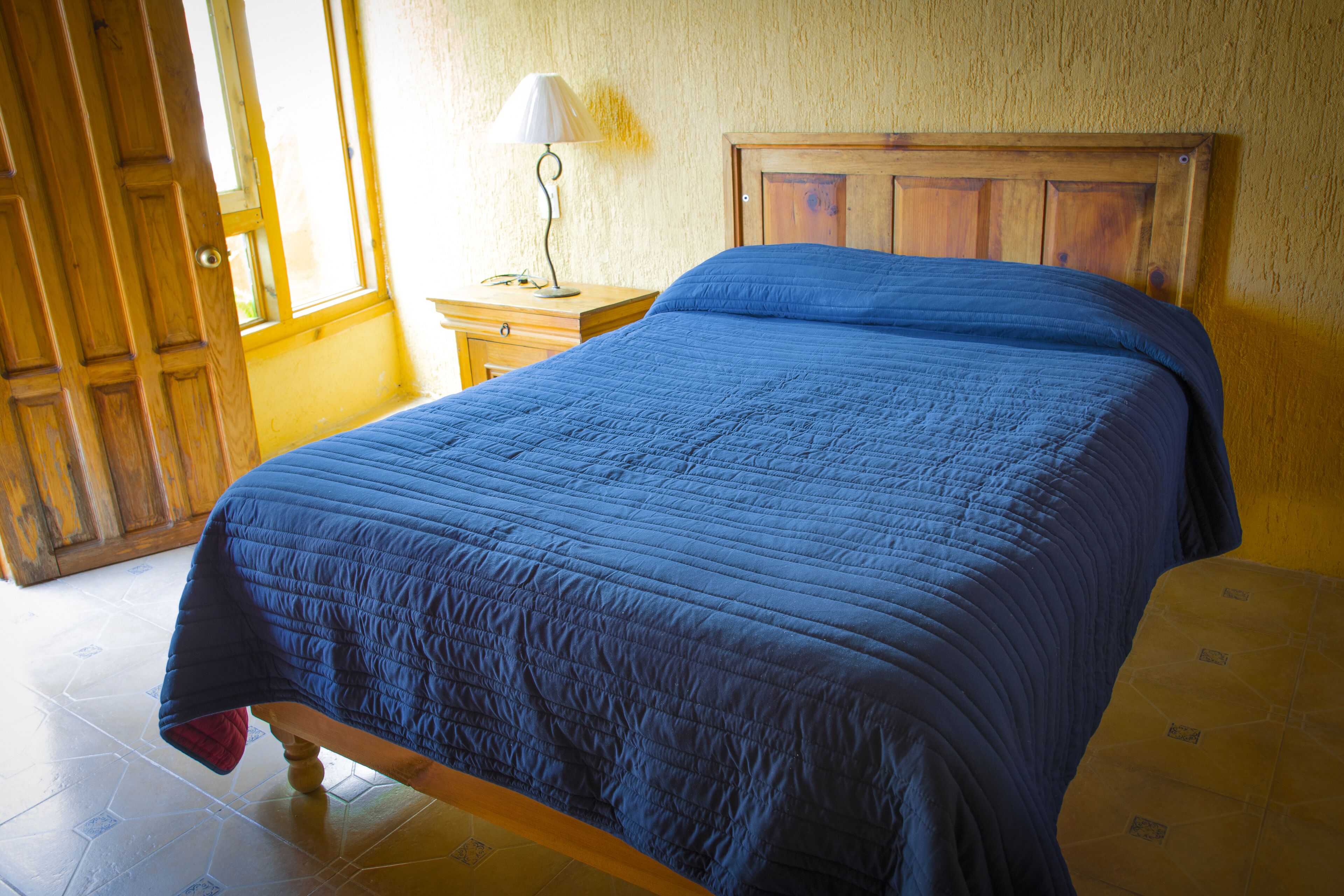 Un dormitorio con una cama de madera, una mesita de noche, una lámpara y un ventanal con vistas al exterior.