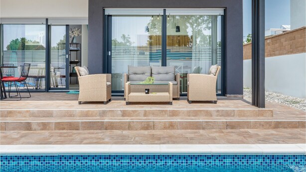 An outdoor patio with wicker furniture, a pool, and a glass door leading to a covered area. - Beach front home in Peroj (Peroj)