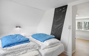 Une chambre avec deux lits, un tableau noir avec des inscriptions, une lampe de chevet et une fenêtre sur laquelle est posé un modèle de voilier.