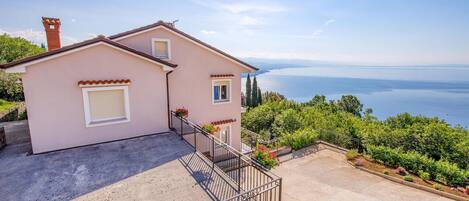 A two-story house with a balcony overlooking a scenic view of the sea and mountains.