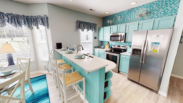 A kitchen with teal cabinets, a central island with bar stools, a refrigerator, and a microwave. - Light and bright 1st floor condo in Sunset Beach | RC 1802 (Sunset Beach)