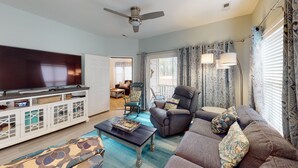 A living room with a flat-screen TV, a sofa, a rocking chair, and a coffee table. - Light and bright 1st floor condo in Sunset Beach | RC 1802 (Sunset Beach)
