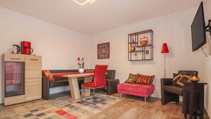 Una sala de estar moderna con una mesa de centro de madera, sillas rojas, un sofá rojo, un tapete estampado y un televisor montado en la pared.