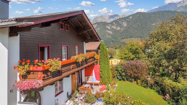 Un chalé tradicional con un balcón decorado con flores coloridas, una terraza de madera y vistas a las montañas.
