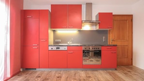Una cocina compacta con armarios rojos, una campana extractora de acero inoxidable, un horno empotrado y una puerta de madera.