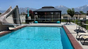 En swimmingpool med en vattenrutschkana, solstolar och en paviljong med utsikt över bergen.