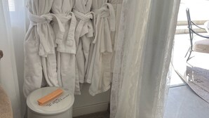 Ett badrum med vita handdukar hängda på en ställning, en korg med hopvikta handdukar och en toalettpappershållare med en rulle på.