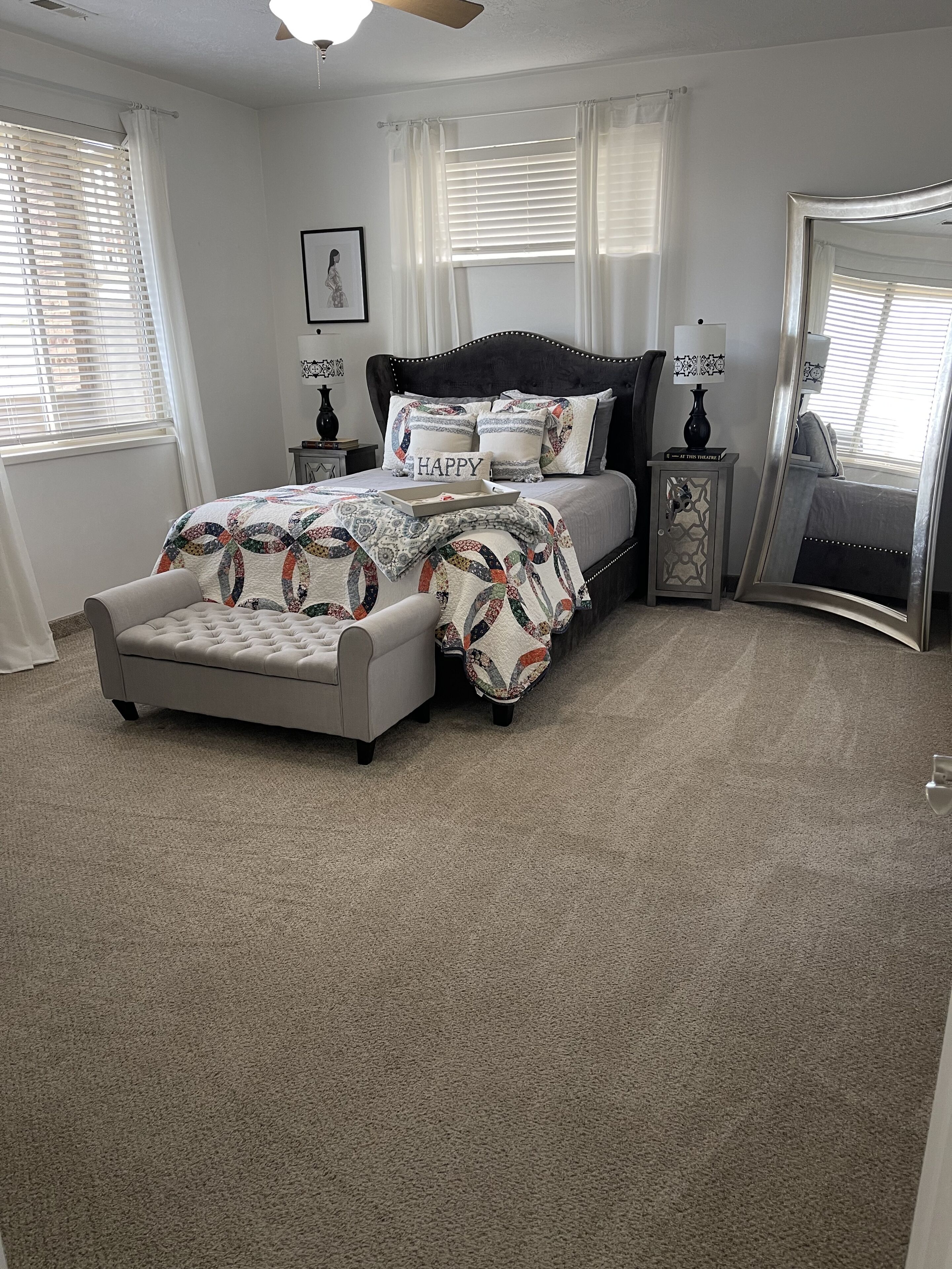 A bedroom with a bed, a nightstand, a mirror, and a window with blinds.