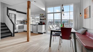Eine moderne Küche mit weißen Schränken, ein Essbereich mit einem Holztisch und roten Stühlen sowie ein rotes Sofa.