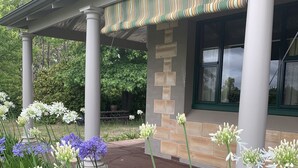 A building with a covered porch supported by columns, a stone wall, and a window with a green frame. - Resort style home set among boutique vineyards. (Summertown)