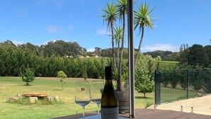 A table with a bottle of wine and two glasses on a covered patio overlooking a grassy field with trees and a fence. - Resort style home set among boutique vineyards. (Summertown)