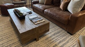 A living room with a brown leather sofa, a wooden coffee table with magazines, and a patterned rug. - 2 Master Bedrooms, Luxury beds, Pool & Hot Tub, Large TVs, Surround Sound (Scottsdale)