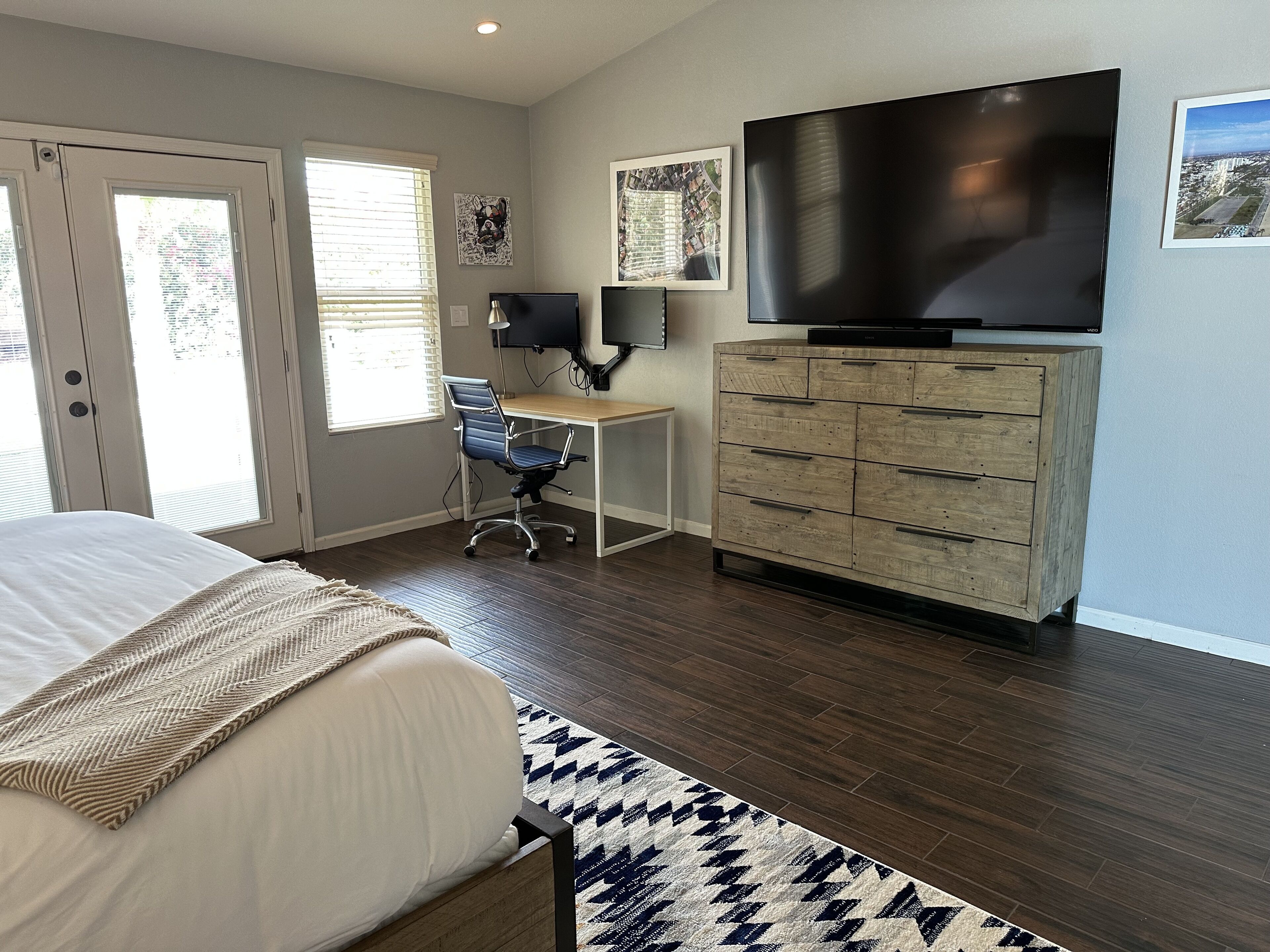 A bedroom with a bed, a desk, a chair, a TV, and a dresser.