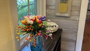 Ein hölzerner Empfangstresen mit einer Vase bunter Blumen, einem Schild mit der Aufschrift 'Welcome' und einem Schild mit der Aufschrift 'Key West' darüber.