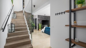 A modern staircase with wooden steps and glass railings, leading to a living area with a blue sofa and a flat-screen TV. - Beautiful home in Sivati with sauna (Sivati)