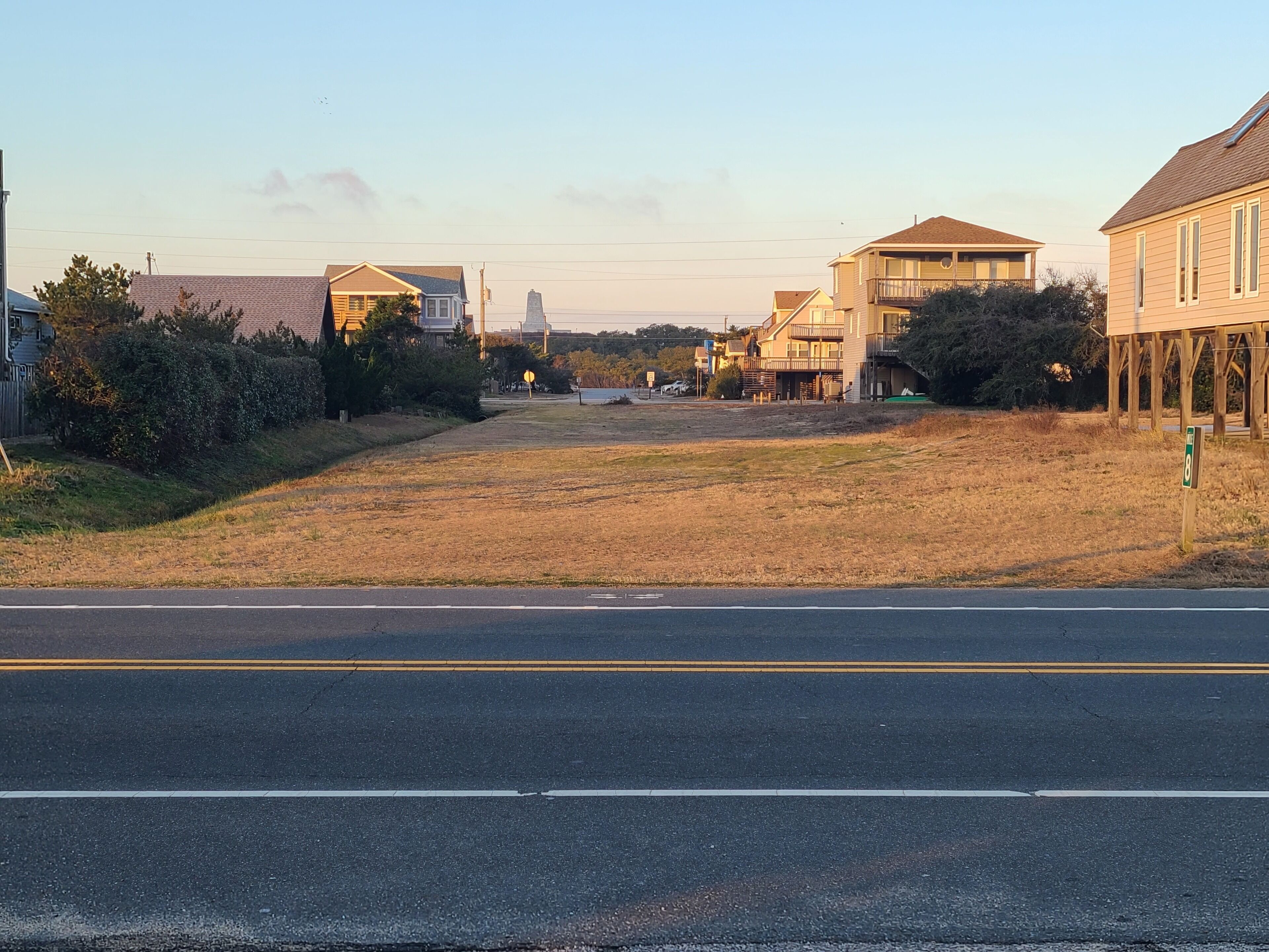 A residential street with houses on both sides, a grassy median, and a clear sky.