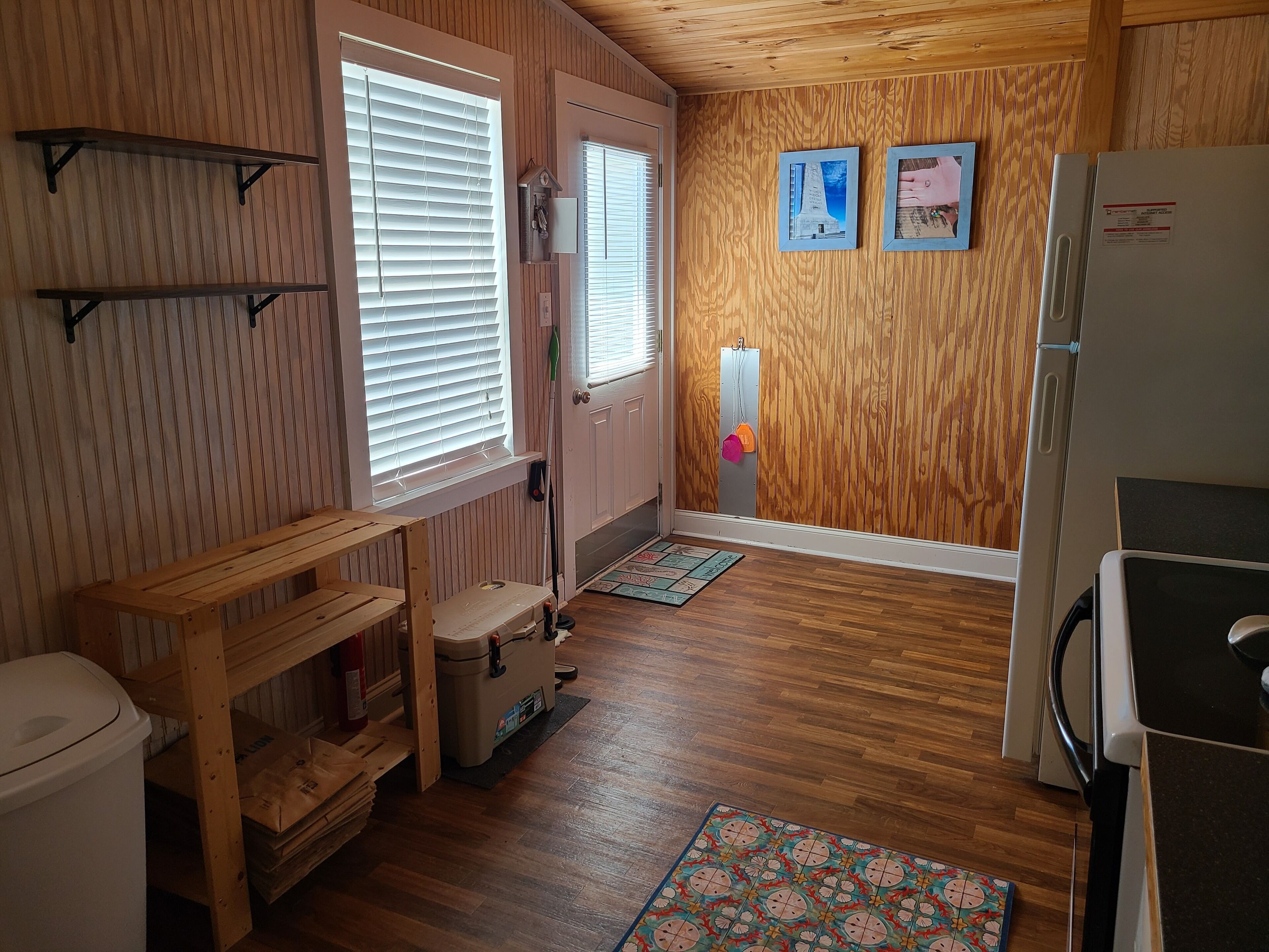 A compact kitchen with wooden walls, a refrigerator, a sink, and a wooden bench.