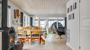 A cozy interior with a wood-burning stove, wooden chairs, a dining table, and a large window offering a view of the outdoors. - Gorgeous home in Glesborg with kitchen (Glesborg)