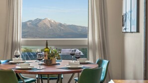 Une table à manger avec vue sur la montagne, une bouteille de vin et un vase rempli de fleurs.