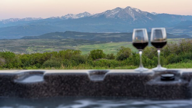 Deux verres de vin rouge posés sur une corniche en pierre, avec un paysage montagneux en arrière-plan.