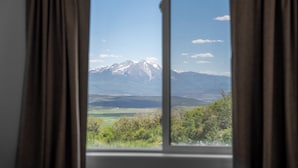 Une fenêtre donnant sur une chaîne de montagnes et un paysage verdoyant.