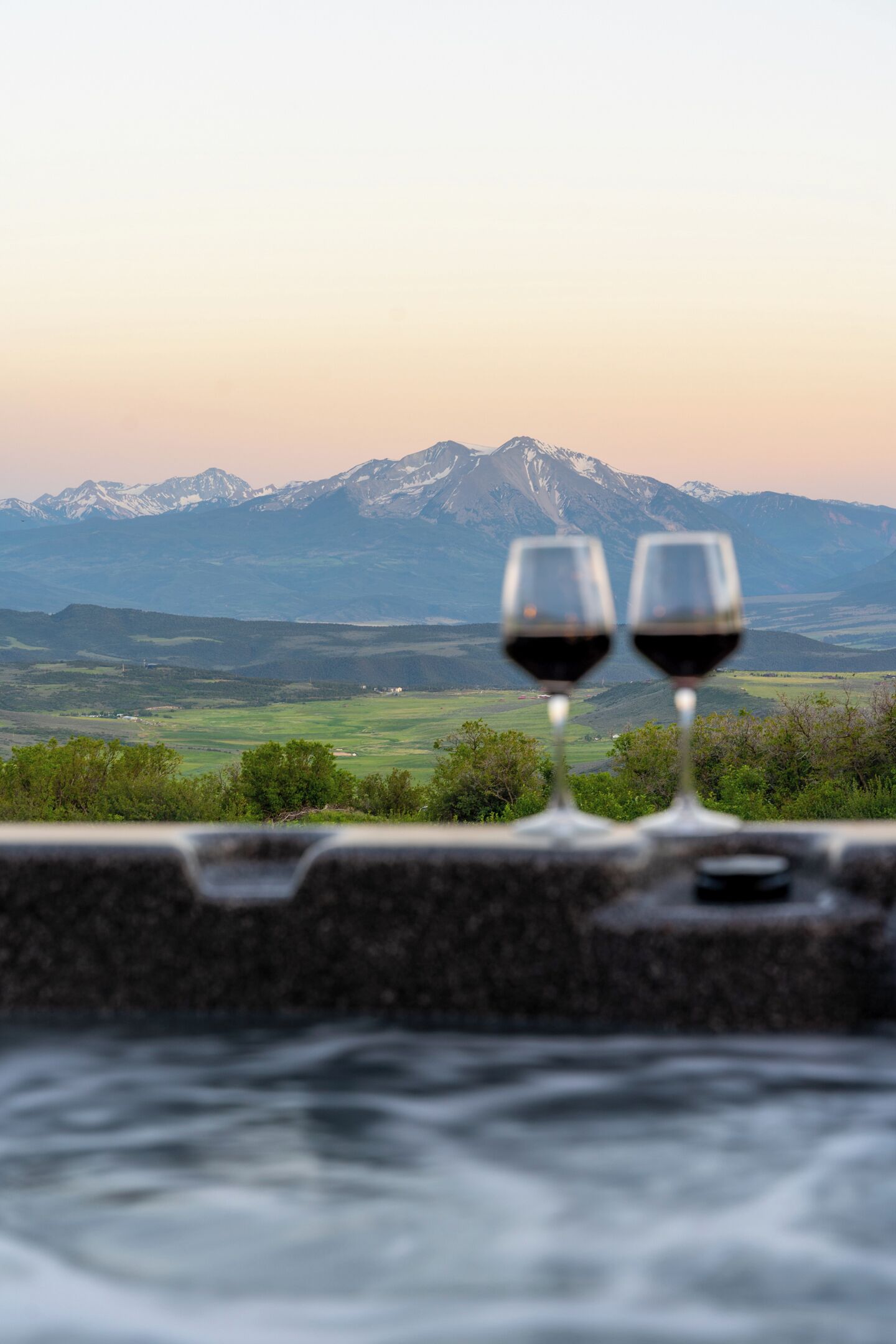 Due bicchieri di vino su una mensola, con un paesaggio montuoso sullo sfondo.