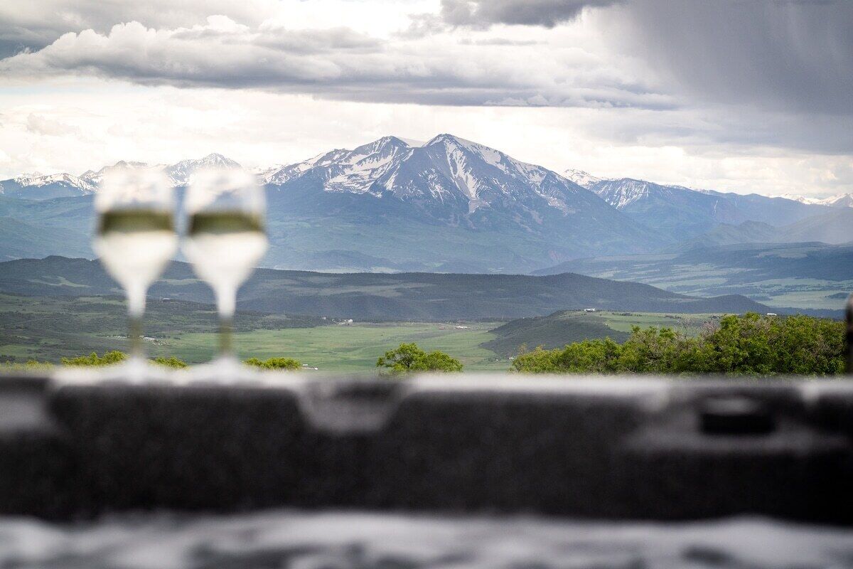 A mountain landscape with two glasses of wine in the foreground.