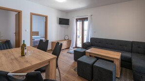 Un salon moderne comprenant un canapé, une table à manger avec des chaises, une petite télévision et un balcon avec une porte coulissante.