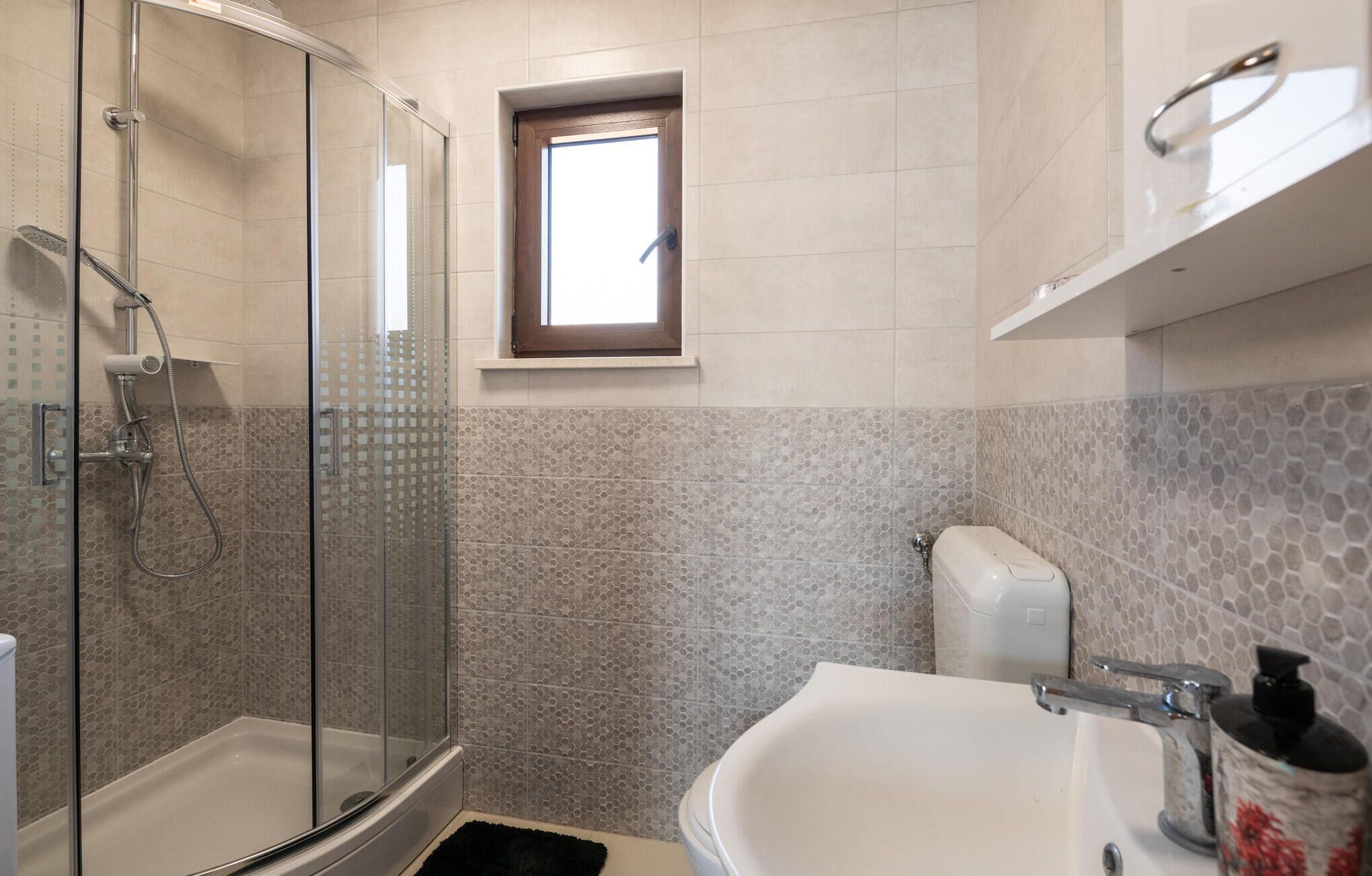 Un baño con ducha de vidrio, bañera blanca y una ventana pequeña.