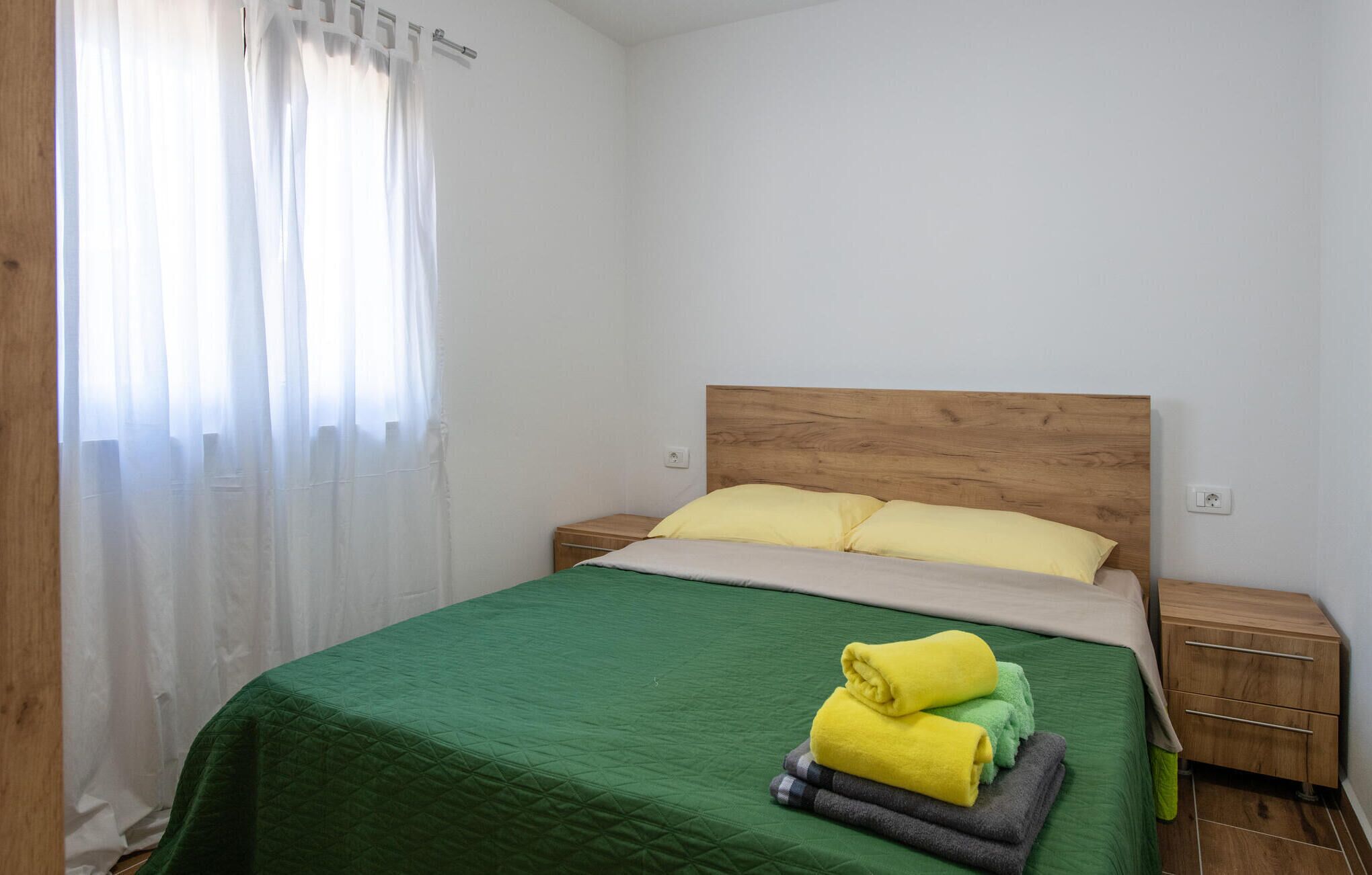 A neatly made bed with a green bedspread and two pillows, a wooden headboard, and a nightstand with a lamp.