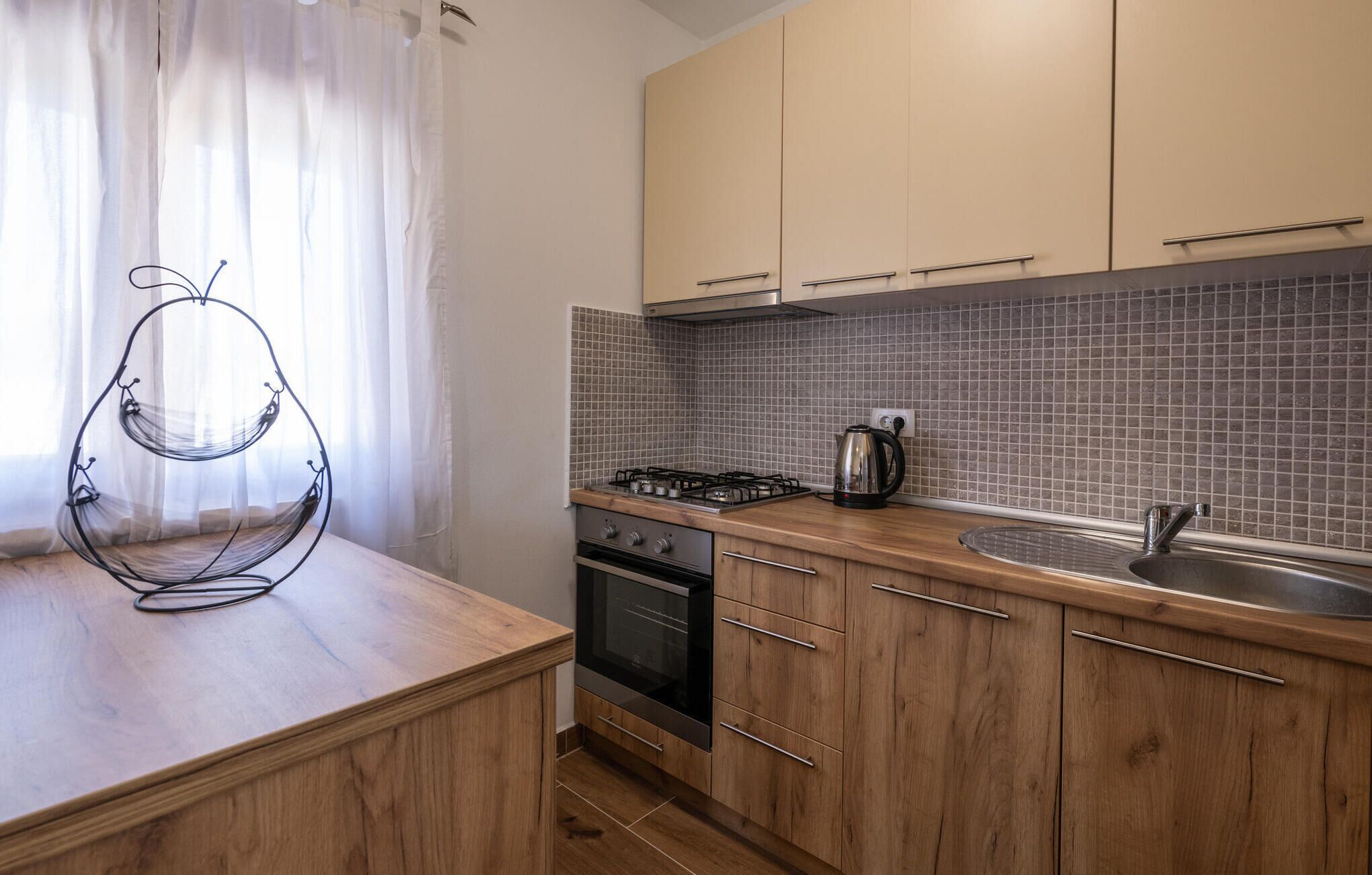 A modern kitchen with wooden cabinets, a gas stove, a kettle, and a sink.