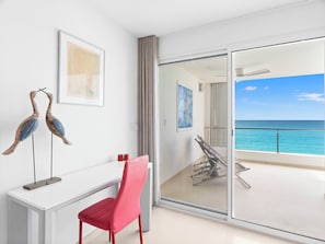 A room with a white desk, a red chair, two wooden bird sculptures, and a view of the ocean through a glass door. - NEW STUNNING VILLA, VILLA SONRISA, BEACHFRONT_OCEAN VIEW (Sint Maarten)