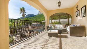 Ein Balkon mit schmiedeeisernem Geländer, Korbmöbeln und Blick auf eine gebirgige Landschaft.