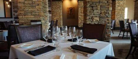 A restaurant with stone walls, white tablecloths, and empty wine glasses.