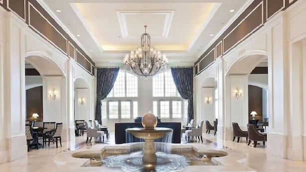 Um saguão imponente com uma fonte central, assentos elegantes e um lustre.