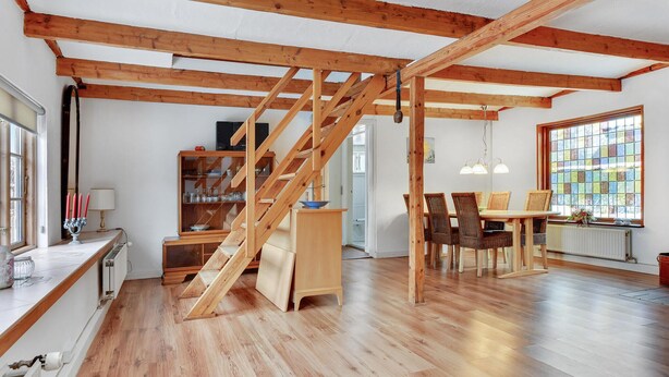 Une pièce spacieuse avec un escalier en bois, un coin repas avec des chaises en osier et une grande fenêtre donnant sur un beau paysage.
