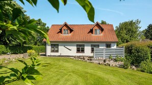 Une maison à deux étages, avec un toit recouvert de tuiles rouges, des murs blancs et un petit jardin devant.