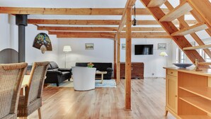 Un salon spacieux avec un plafond en bois, un canapé noir, une table basse blanche et un meuble en bois.