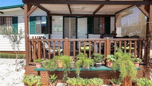 Una veranda de madera con zona de estar techada, rodeada de plantas en macetas.