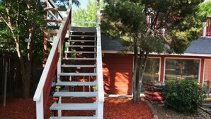 Eine Holztreppe führt zu einer Garage mit roter Tür, umgeben von Rindenmulch und kleinen Steinen.